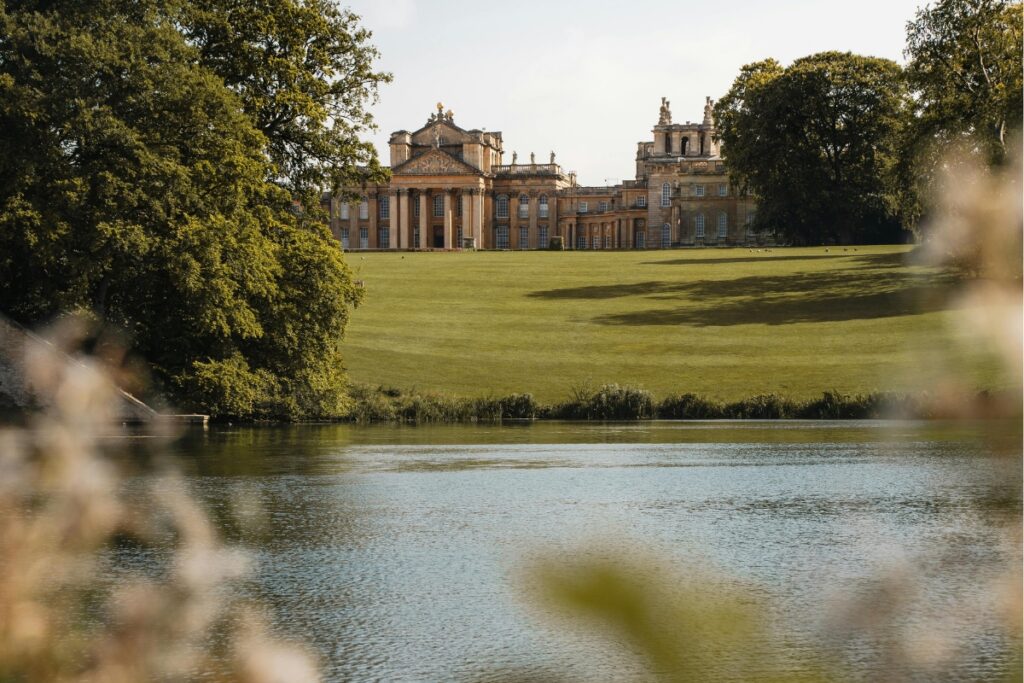 Historic palace viewed across a calm lake with green lawns and trees framing the foreground.