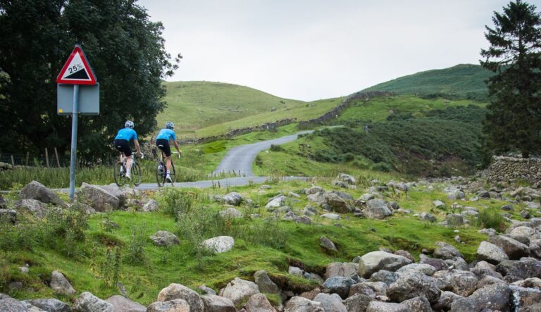 Two cyclists in blue jackets riding up a hill